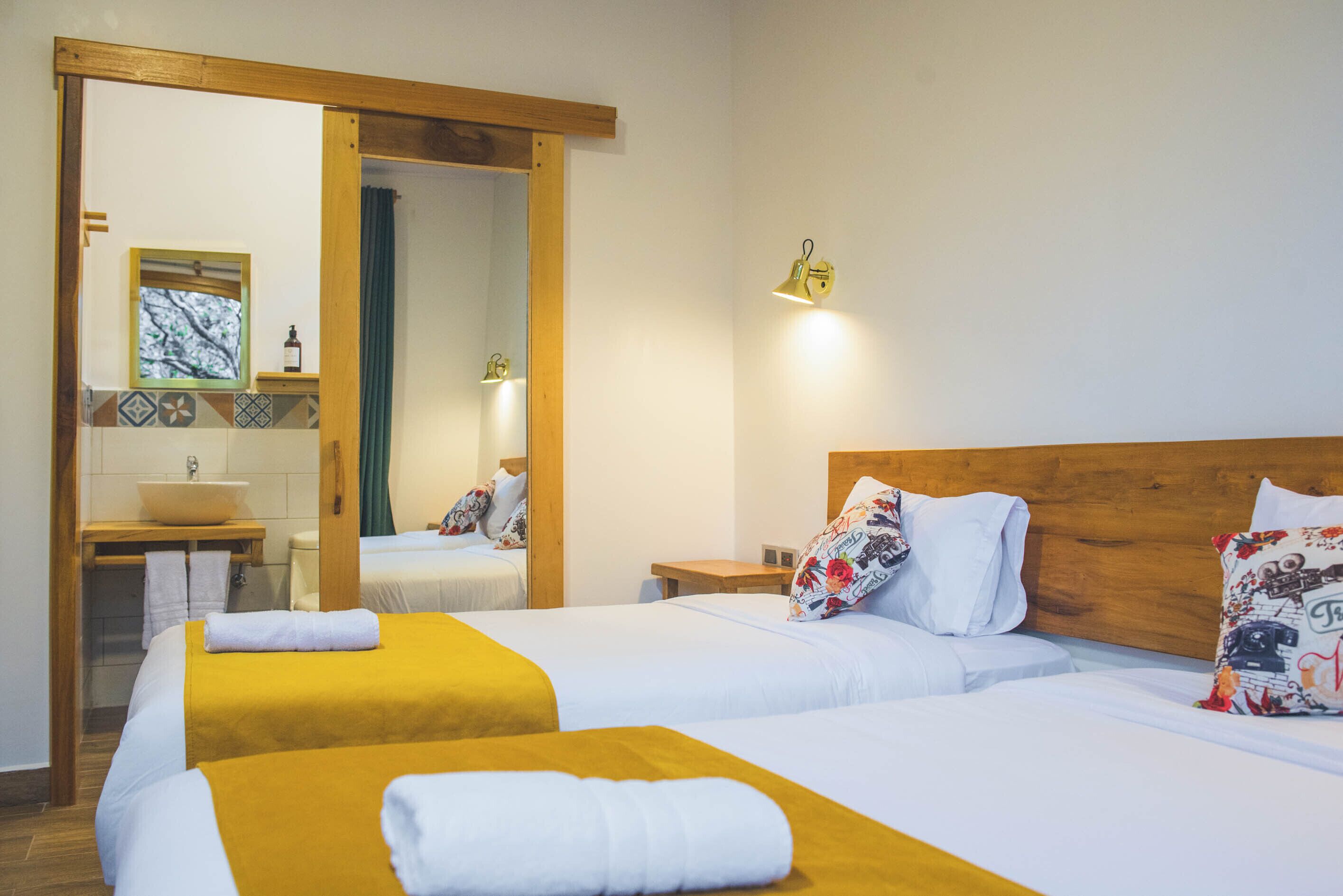 A hotel room with two beds, a wooden headboard, a mirror, a sink, and a window with a view.