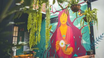 A mural with a central figure holding a flower, surrounded by hanging plants and birds.