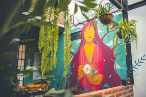 A mural with a central figure holding a flower, surrounded by hanging plants and birds. - Margarit Boutique Hotel (Mindo)