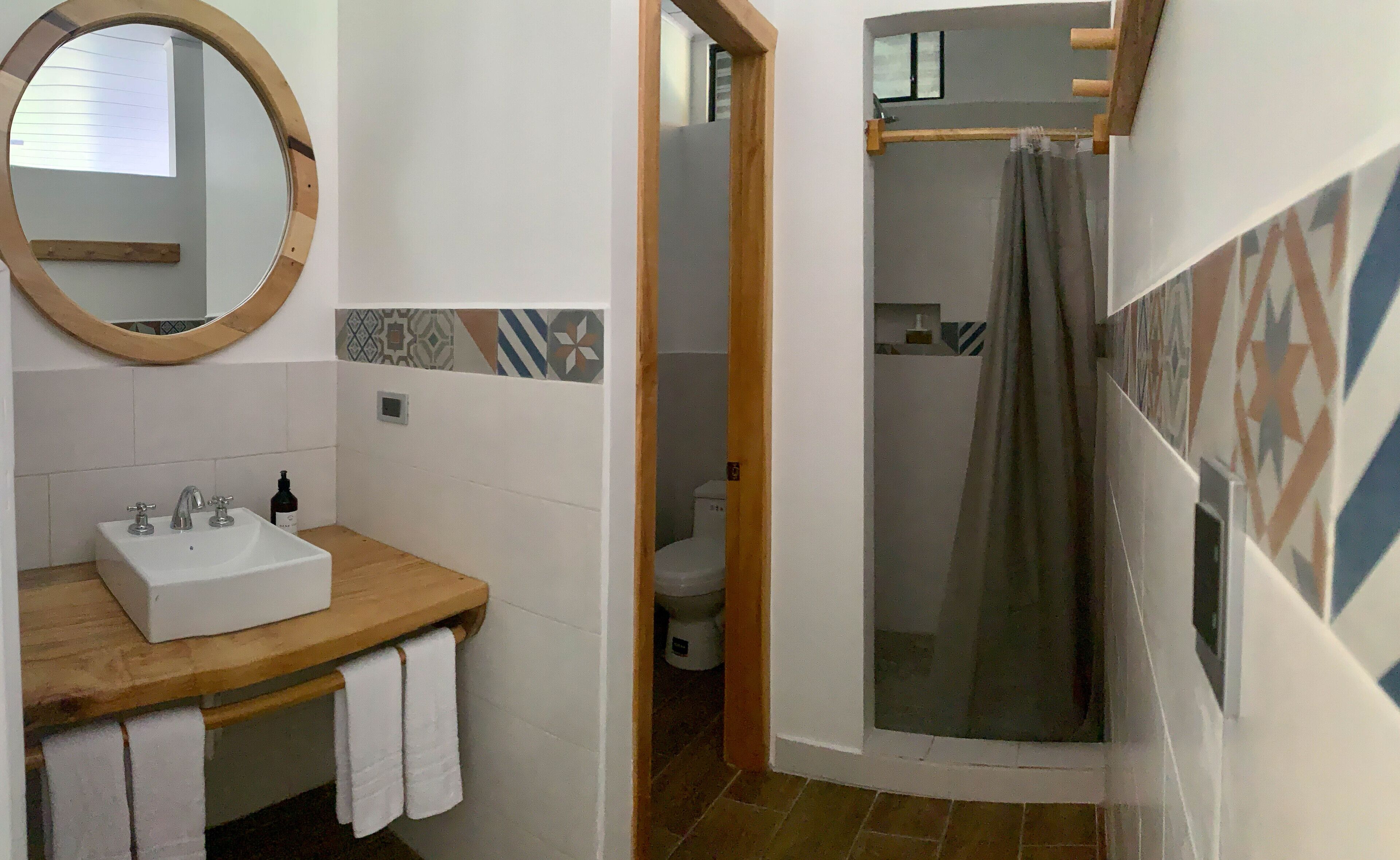 A bathroom with a wooden vanity, a round mirror, and a shower area with a glass door.
