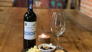 A wooden table with a bottle of Manucura et al. wine, a glass, and a plate of cheese, fruits, nuts, and crackers.