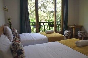A hotel room with two beds, a small table, and a view of greenery through large windows. - Margarit Boutique Hotel (Mindo)