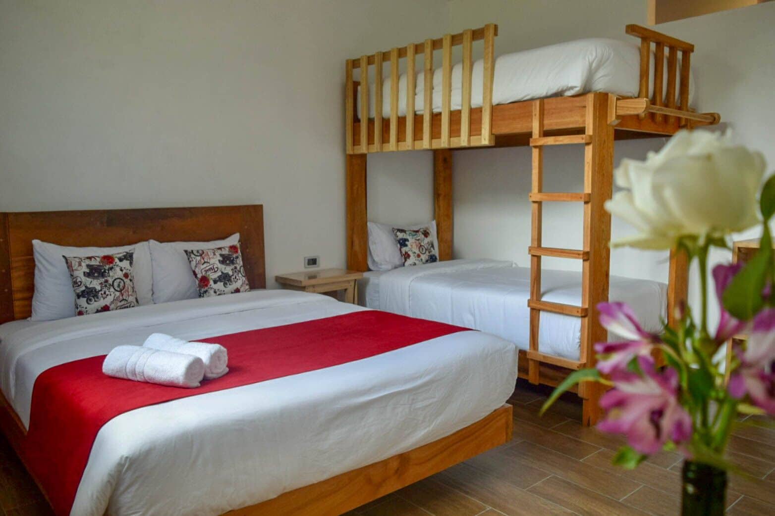 A bunk bed room with two beds, a red blanket, and a white flower vase.