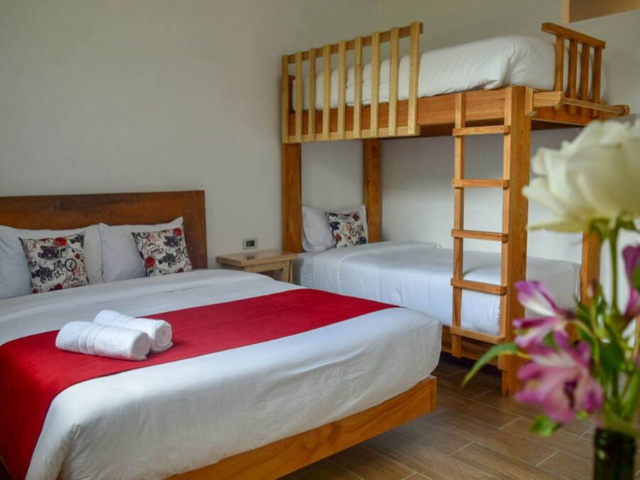 A bunk bed room with two beds, a red blanket, and a white flower vase.