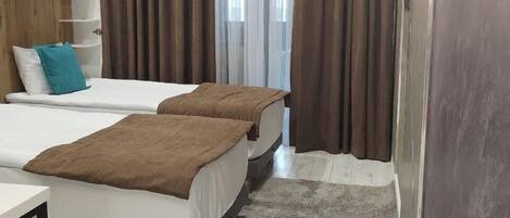 A hotel room with two beds, a desk, a mirror, and a window with curtains.