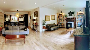 Een ruime woonkamer met een grijze bank, een houten salontafel en een open haard. Er is een boekenkast vol boeken en een potplant.