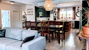 Een moderne keuken met donkere kastjes, een eethoek met houten stoelen, en een grijze bank met een zwart kussen.