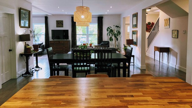 Een ruime eethoek met een grote houten tafel, twee hangende hanglampen en uitzicht op de aangrenzende woonkamer.