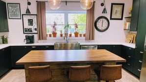Een moderne keuken met een houten kookeiland en barstoelen, een groot raam met planten, een klok en een lijst met een foto aan de muur.