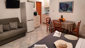Ein kompakter Wohnbereich mit Sofa, Esstisch, Küchenzeile und einem an der Wand befestigten Fernseher.