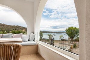 A balcony with a view of a lake and hills, a seating area with cushions, and a stone fence. - Luxury apartment in the best location in Aegina with breathtaking sea view! (AEGINA)