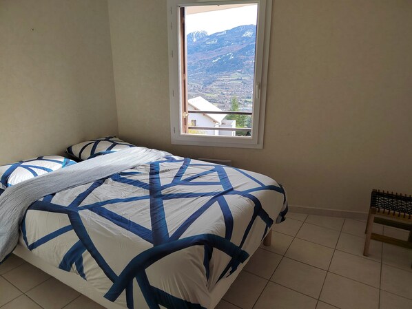 Een slaapkamer met een bed, een raam en uitzicht op een bergachtig landschap.