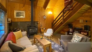 A cozy wooden cabin interior with a fireplace, a sofa, a chair, and a staircase. - Cozy Mt. Baker Cabin, Wi-Fi, Sleeps 6-8, Pets OK (Deming)
