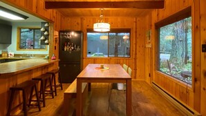 A wooden cabin interior with a kitchen, dining area, and large windows offering a forest view. - Cozy Mt. Baker Cabin, Wi-Fi, Sleeps 6-8, Pets OK (Deming)