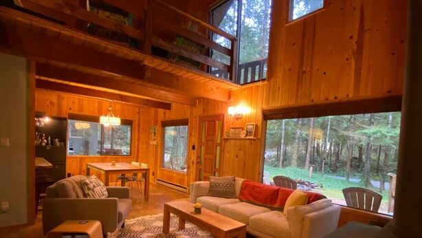 A cozy cabin interior with a living room, dining area, and large windows offering a view of the forest. - Cozy Mt. Baker Cabin, Wi-Fi, Sleeps 6-8, Pets OK (Deming)