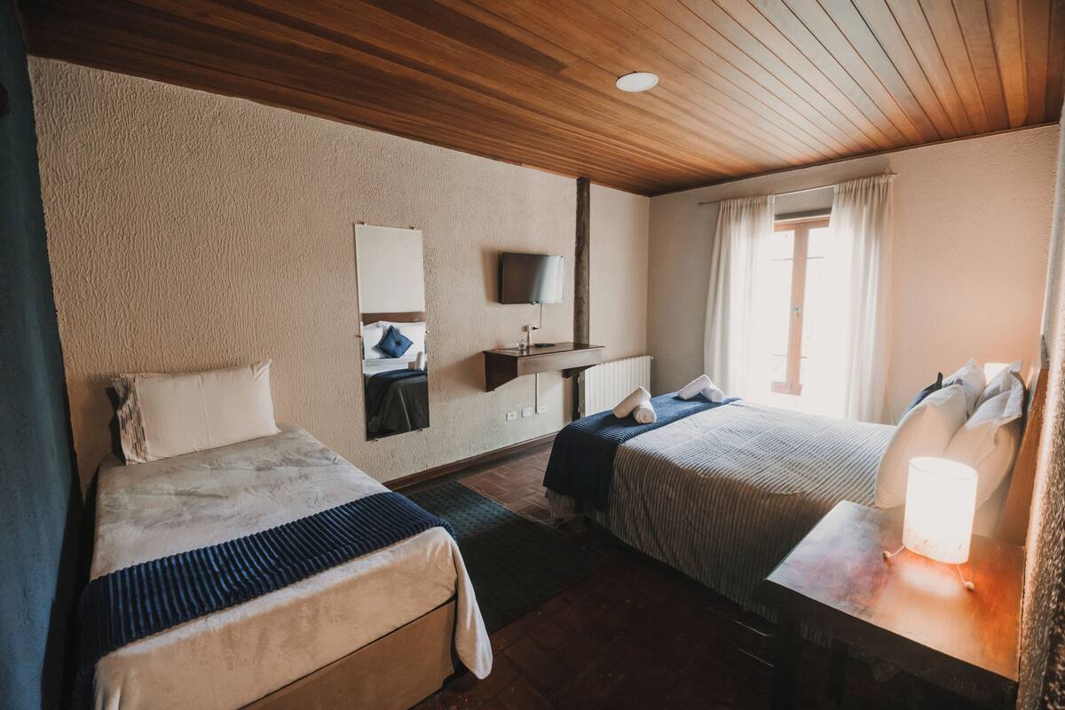 Hotellihuone, jossa on kaksi sänkyä, televisio, työpöytä lampun kanssa ja ikkuna, jossa on verhot.