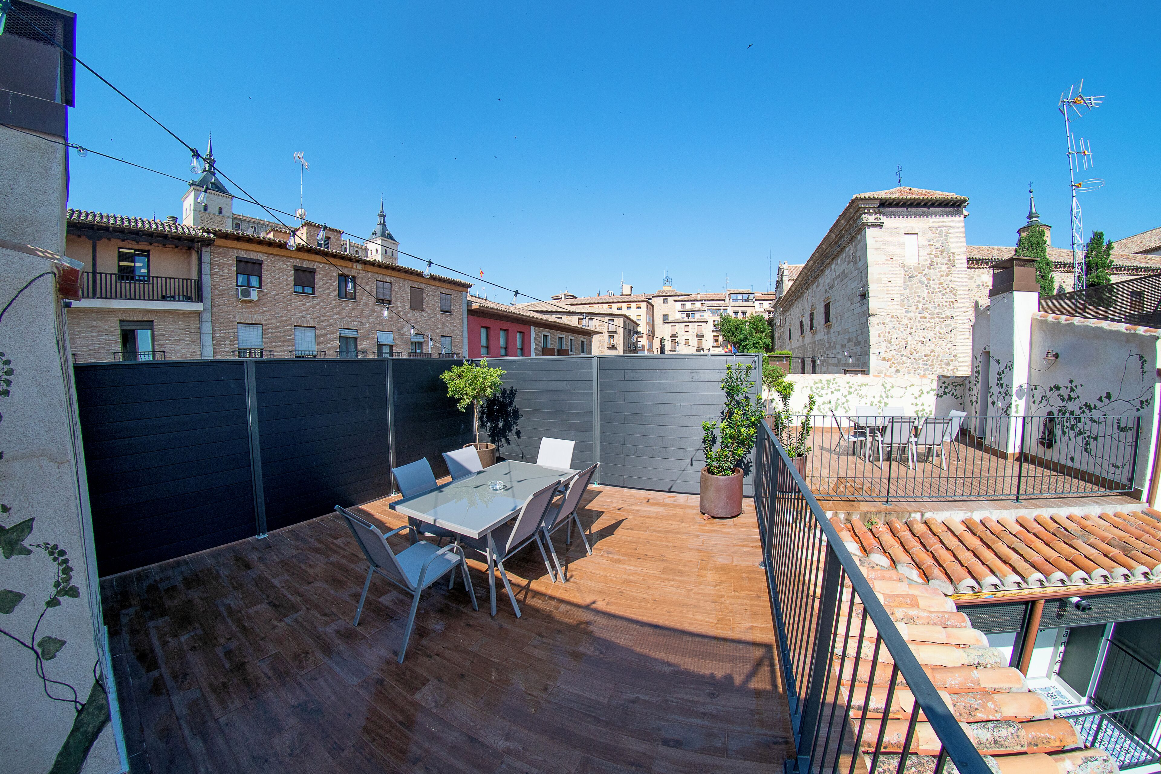 Una terrazza sul tetto con tavolo e sedie, circondata da un basso muro in pietra e piante in vaso.