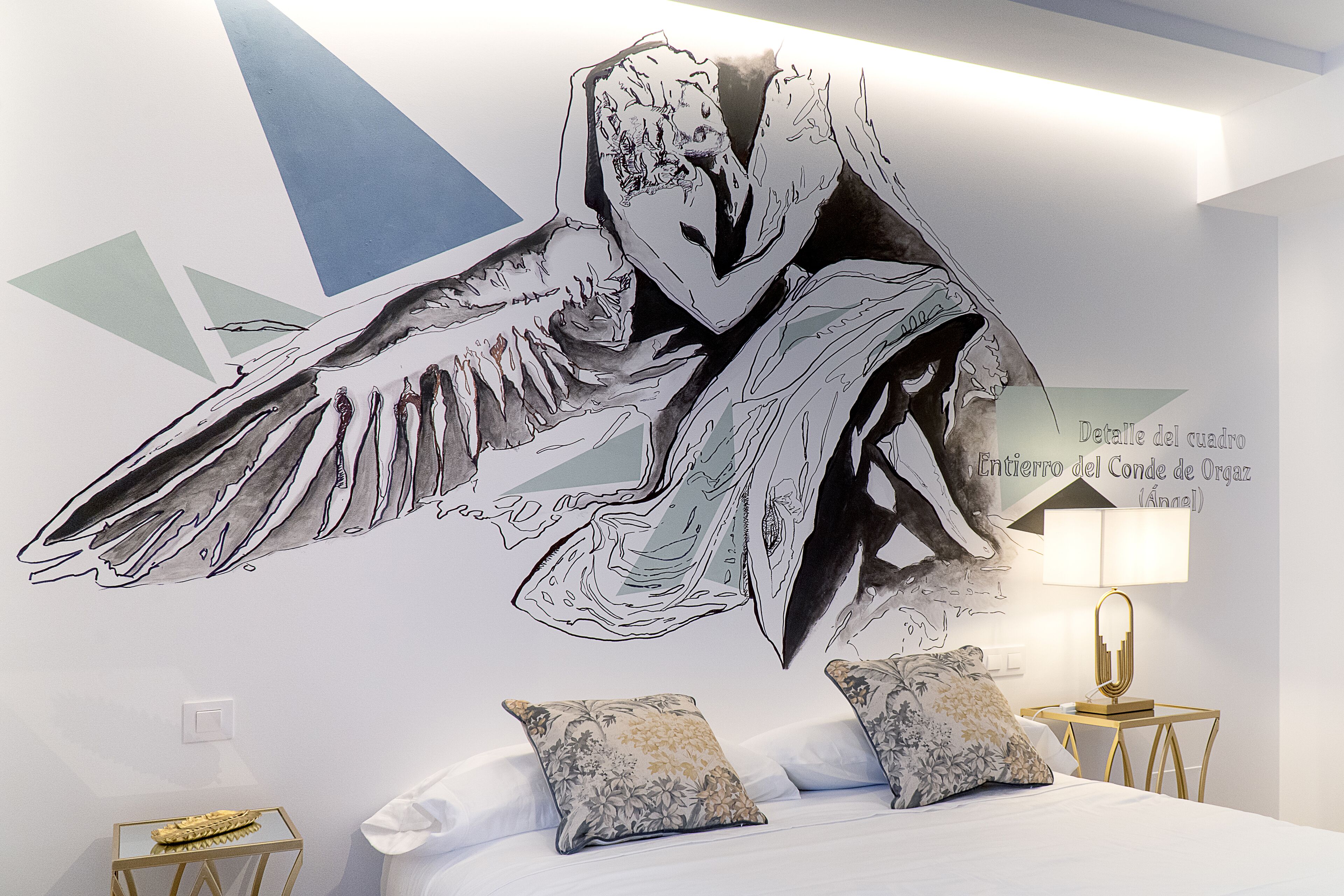 A bedroom with a large wall mural, a bed with pillows, a bedside table with a lamp, and a small side table with a decorative item.