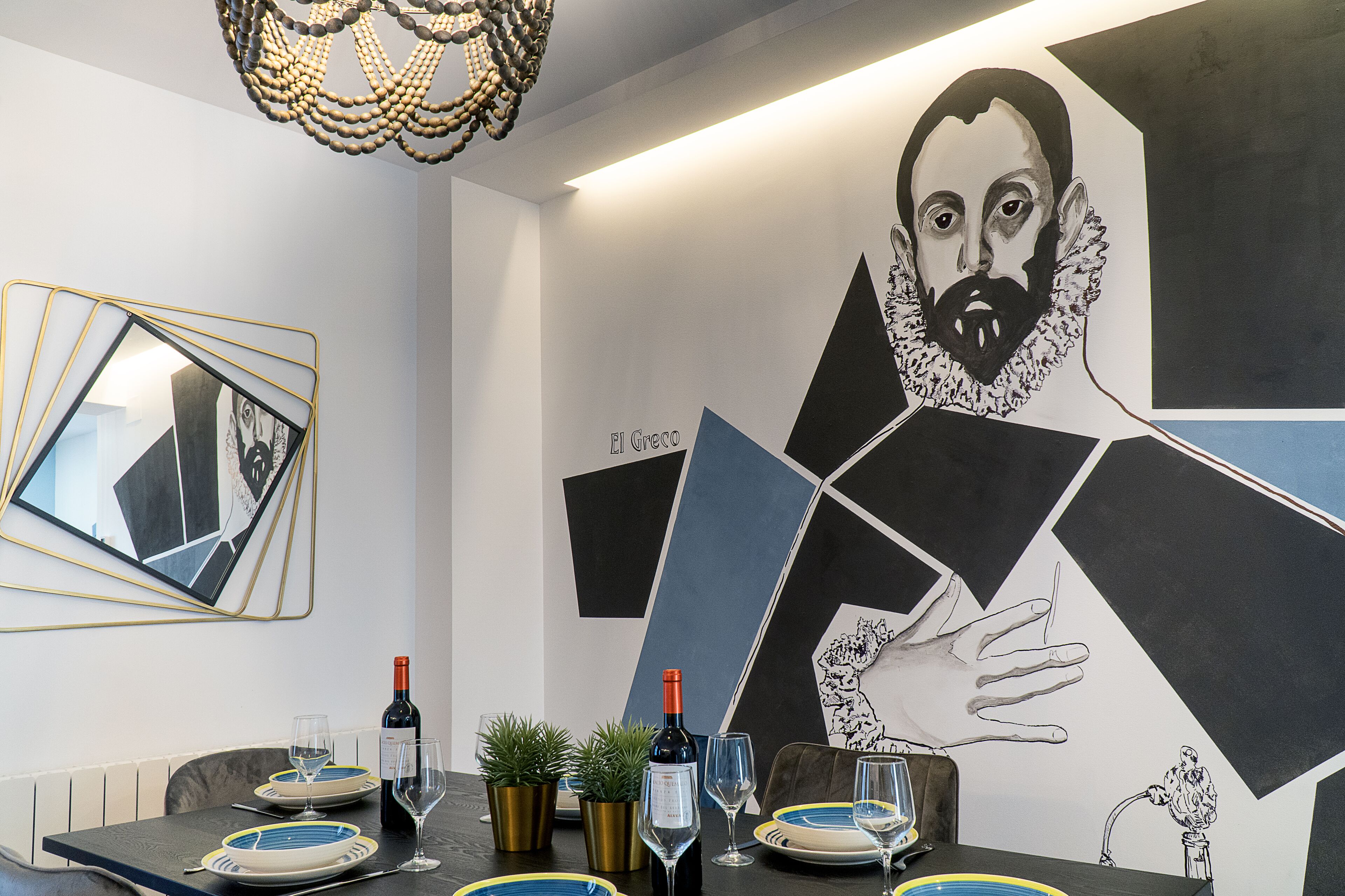 Un espace de salle à manger moderne, agrémenté d’une œuvre d’art murale aux motifs géométriques, d’un lustre et d’une table mise pour le repas.
