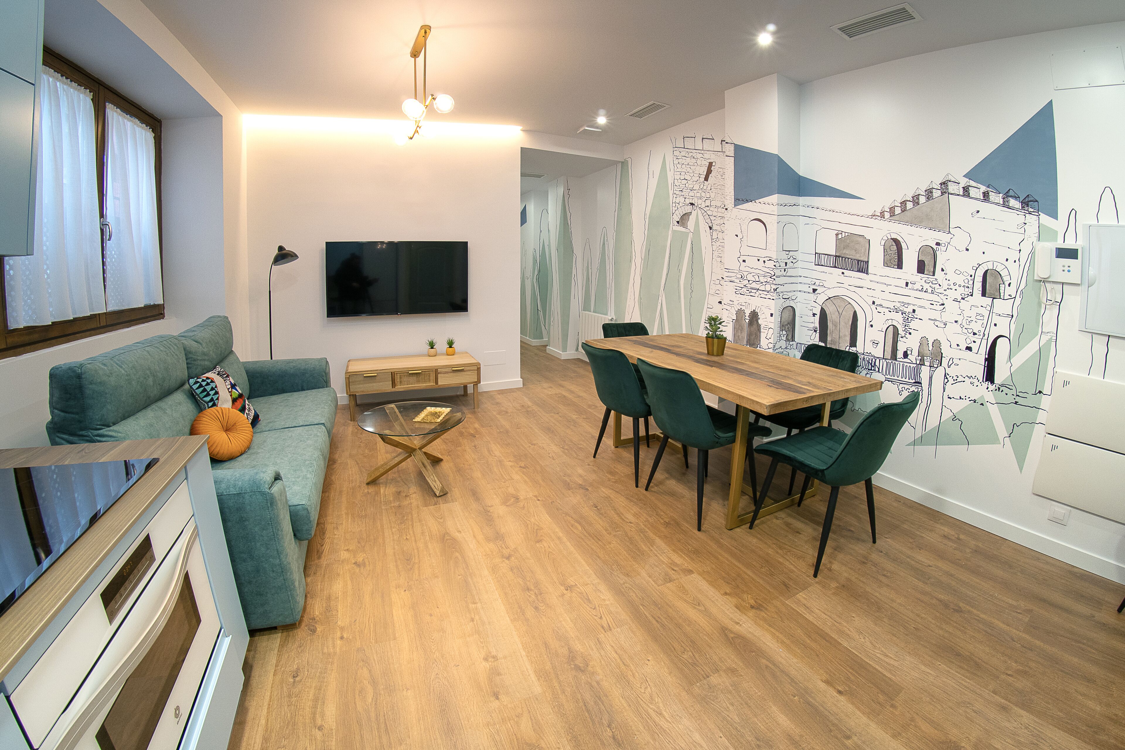 A modern living room with a sofa, a dining table with chairs, a TV, and a mural on the wall.