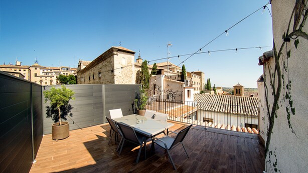 Una terraza en la azotea con una mesa y sillas, rodeada por una cubierta de madera y un muro bajo.