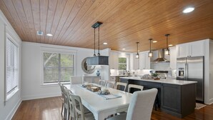 Een moderne keuken met houten plafond, witte kasten, roestvrijstalen apparatuur en een centraal eiland.