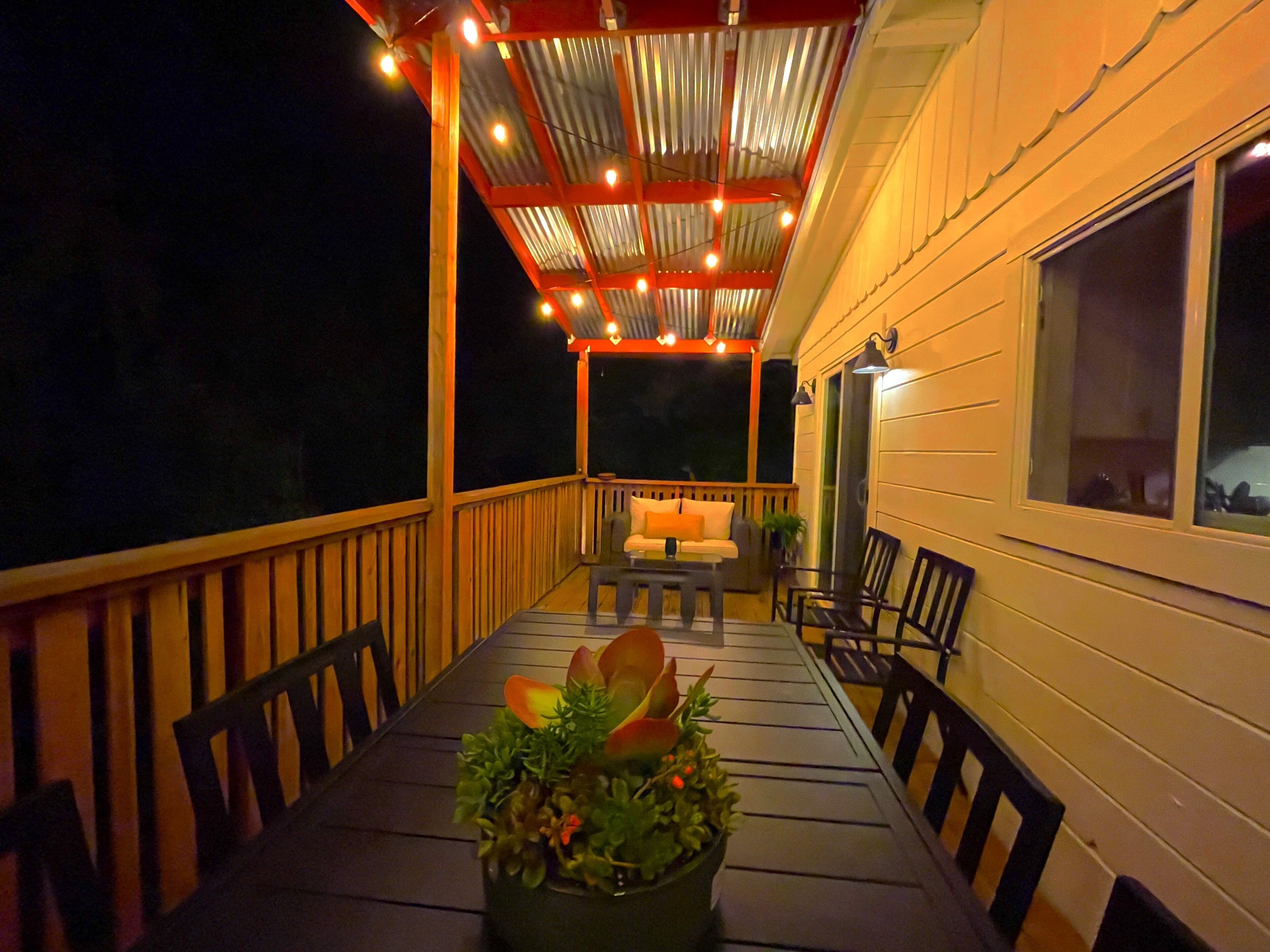 A covered outdoor patio with a table and chairs, string lights, and a potted plant.