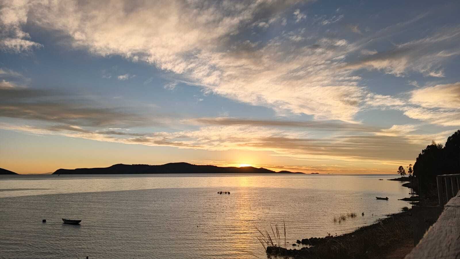 A calm body of water with a sunset, boats, and a distant shoreline.