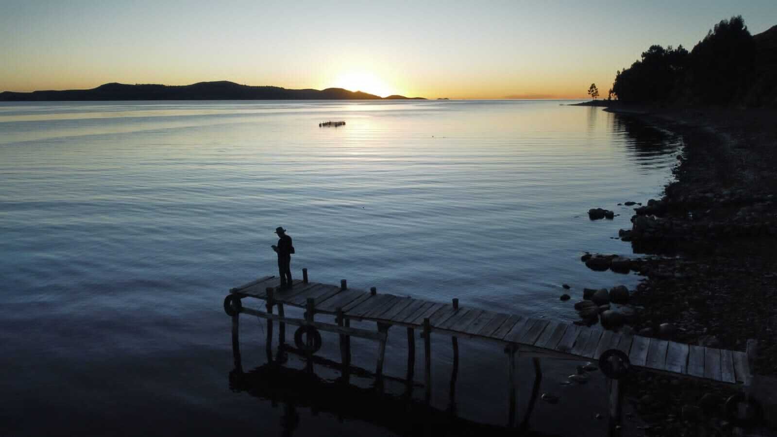 A calm lake at sunset with a wooden dock extending into the water.