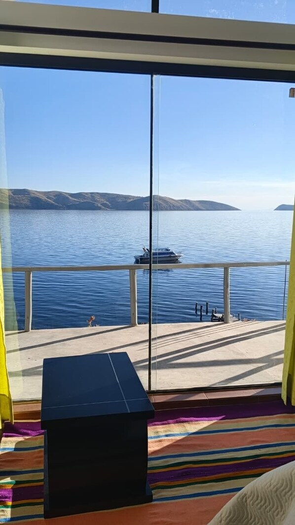 A room with a large glass window overlooking a body of water, a bench, and a colorful rug. - LUNA DEL TITIKAKA LODGE (Moon Island)
