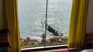 A room with a large window, a wooden floor, and a colorful striped rug. - LUNA DEL TITIKAKA LODGE (Moon Island)