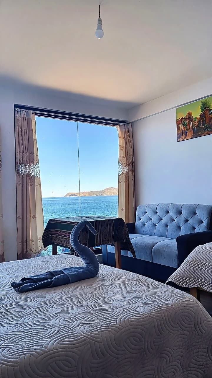 A room with a bed, a blue sofa, a painting, and a view of the sea.