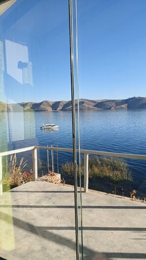 A view of a lake with a boat, a clear sky, and a concrete deck with a railing. - LUNA DEL TITIKAKA LODGE (Moon Island)