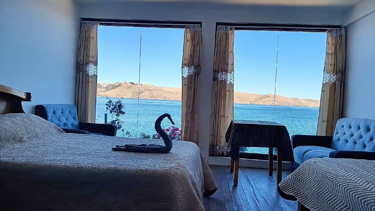 A hotel room with a bed, a table, and a chair, with a view of the sea and hills.