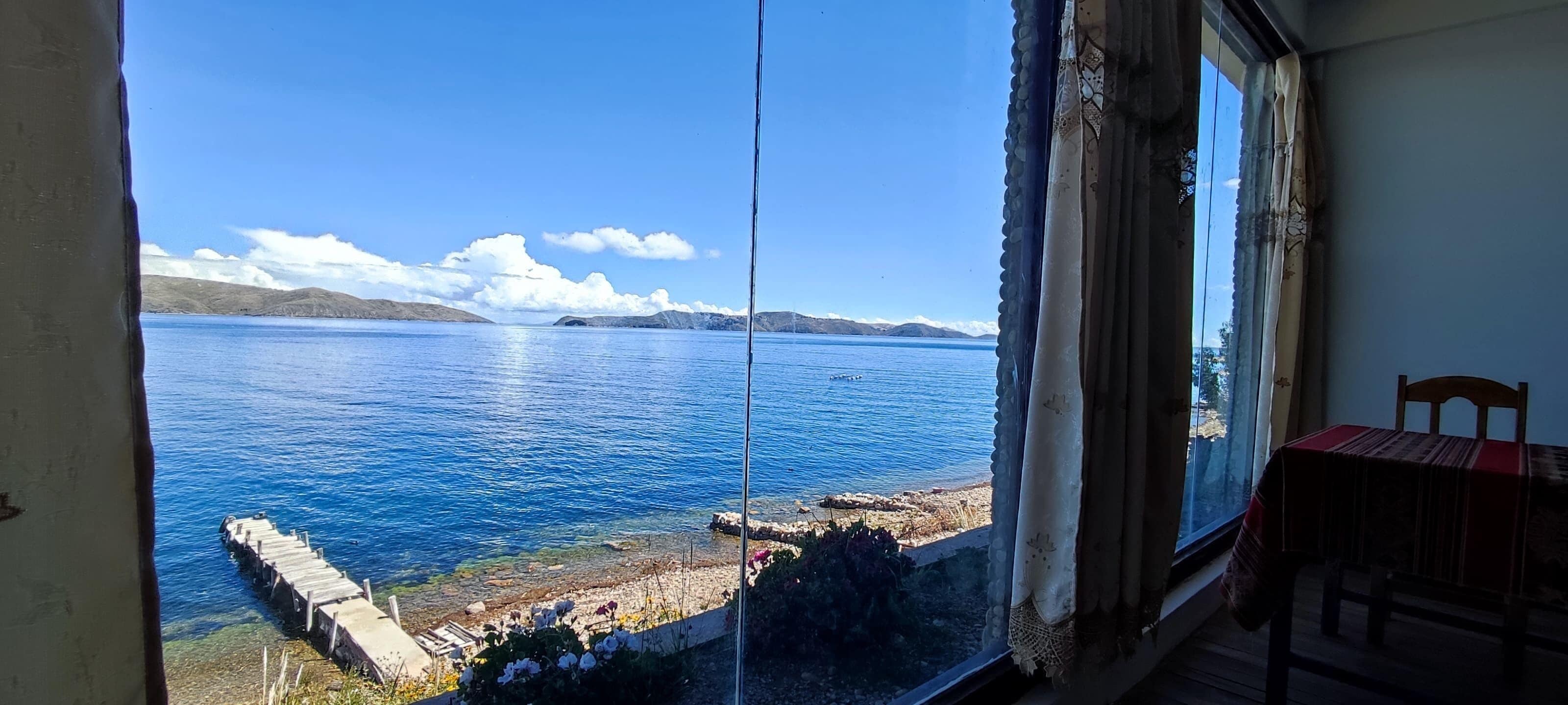Una habitación con un gran ventanal con vistas a un lago, una mesa de madera y una silla.