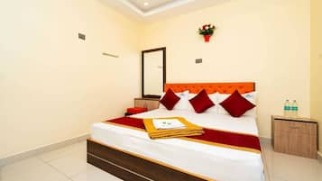Una habitación de hotel con una cama, una mesita de noche, un espejo y una pequeña mesa con botellas.