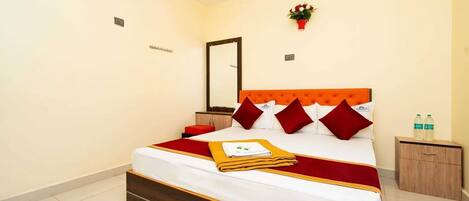 A hotel room with a bed, a nightstand, a mirror, and a small table with bottles.