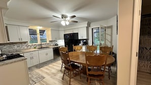Een moderne keuken met witte kasten, een granieten aanrechtblad en een eethoek met houten stoelen.