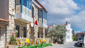 A traditional building with a stone facade, blue-framed windows, and a red flag. - Lamur Otel (Cesme)