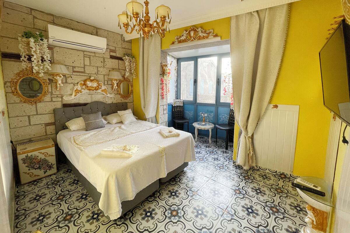 A bedroom with a bed, a chandelier, a mirror, and a window with curtains.