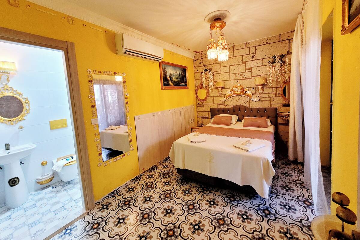 A bedroom with a bed, a mirror, a chandelier, and a brick wall.