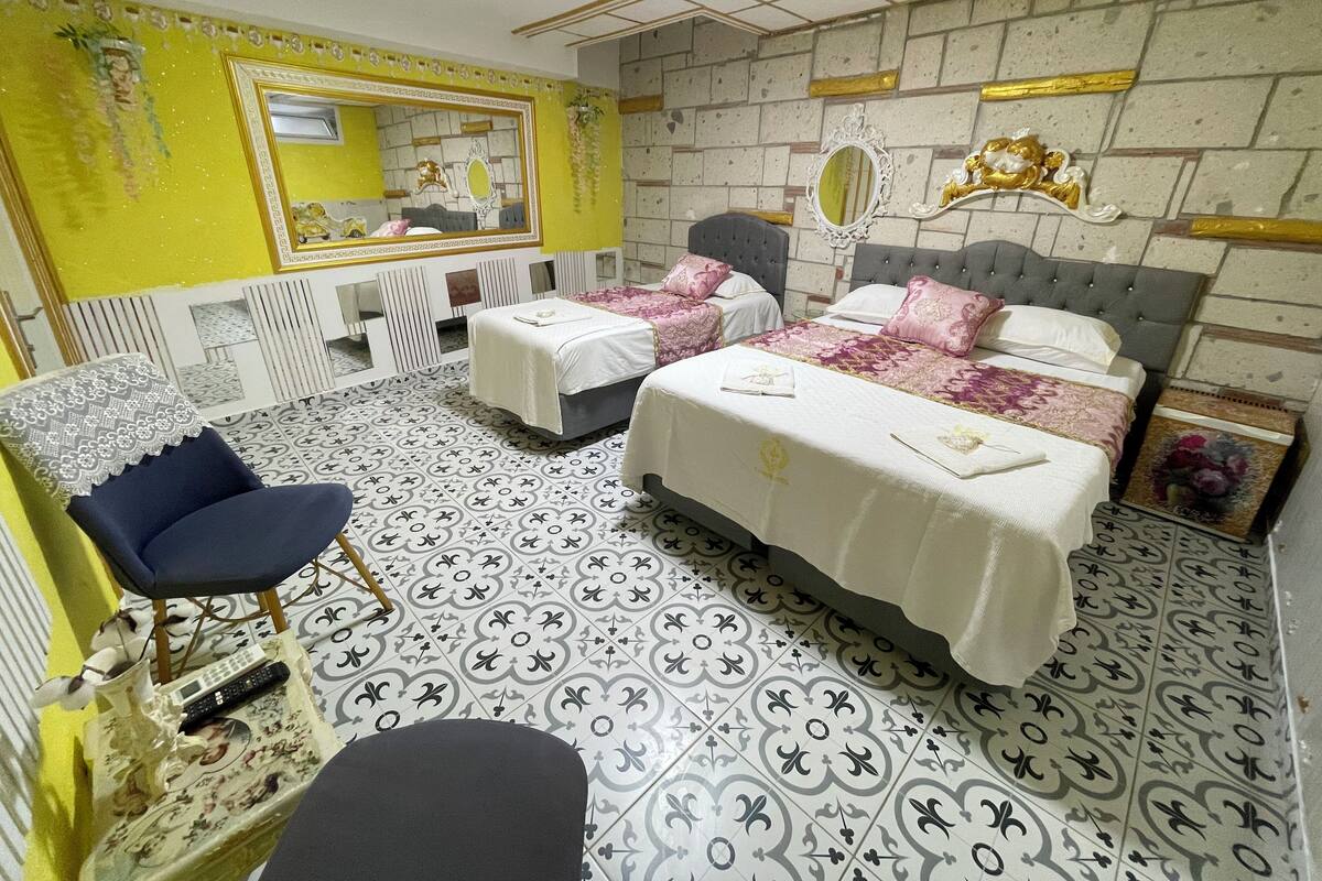 A hotel room with two beds, a chair, a mirror, and a patterned floor.