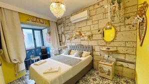 A bedroom with a large bed, a chandelier, a mirror, and a brick-patterned wall. - Lamur Otel (Cesme)
