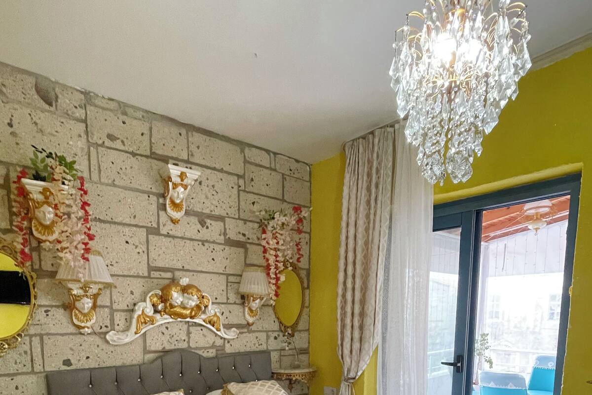 A bedroom with a bed, a chandelier, a mirror, and a view of the outside.