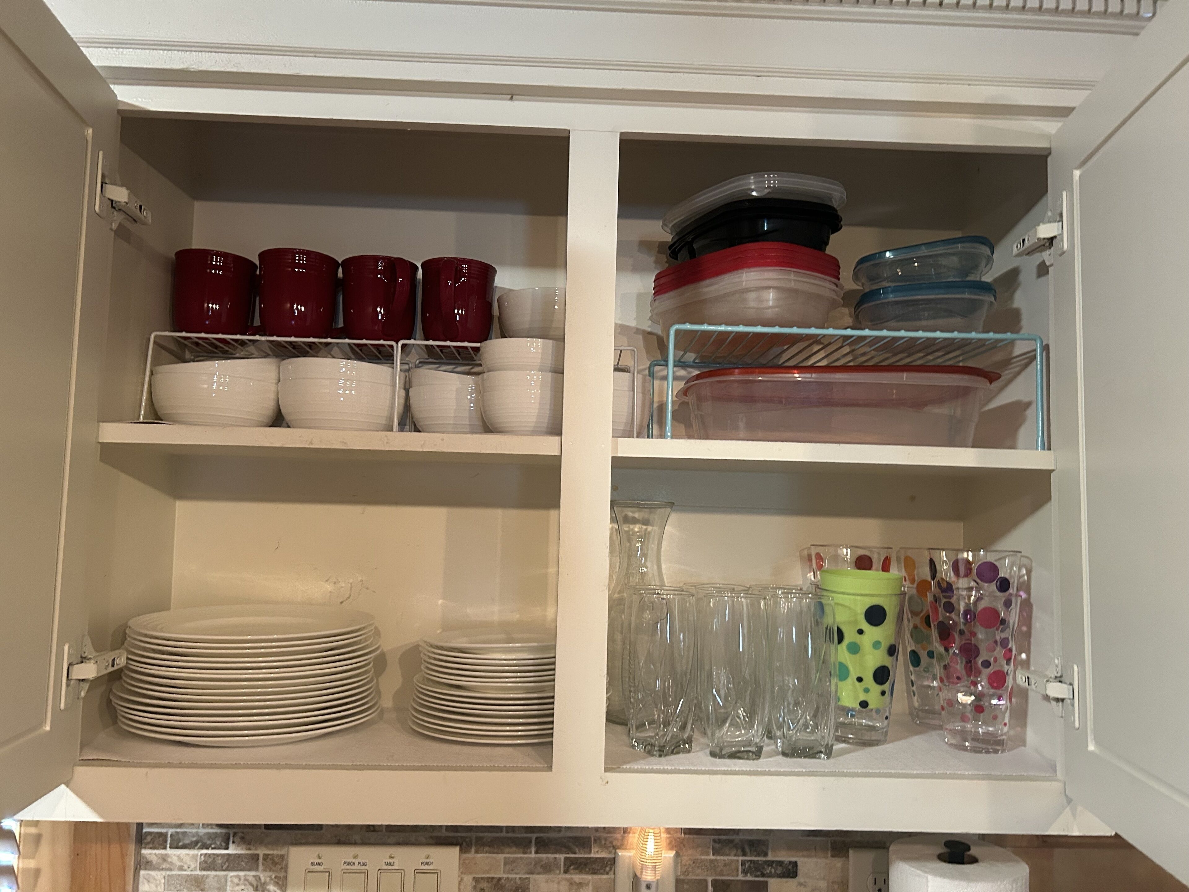 A kitchen cabinet with shelves containing plates, bowls, and glassware.