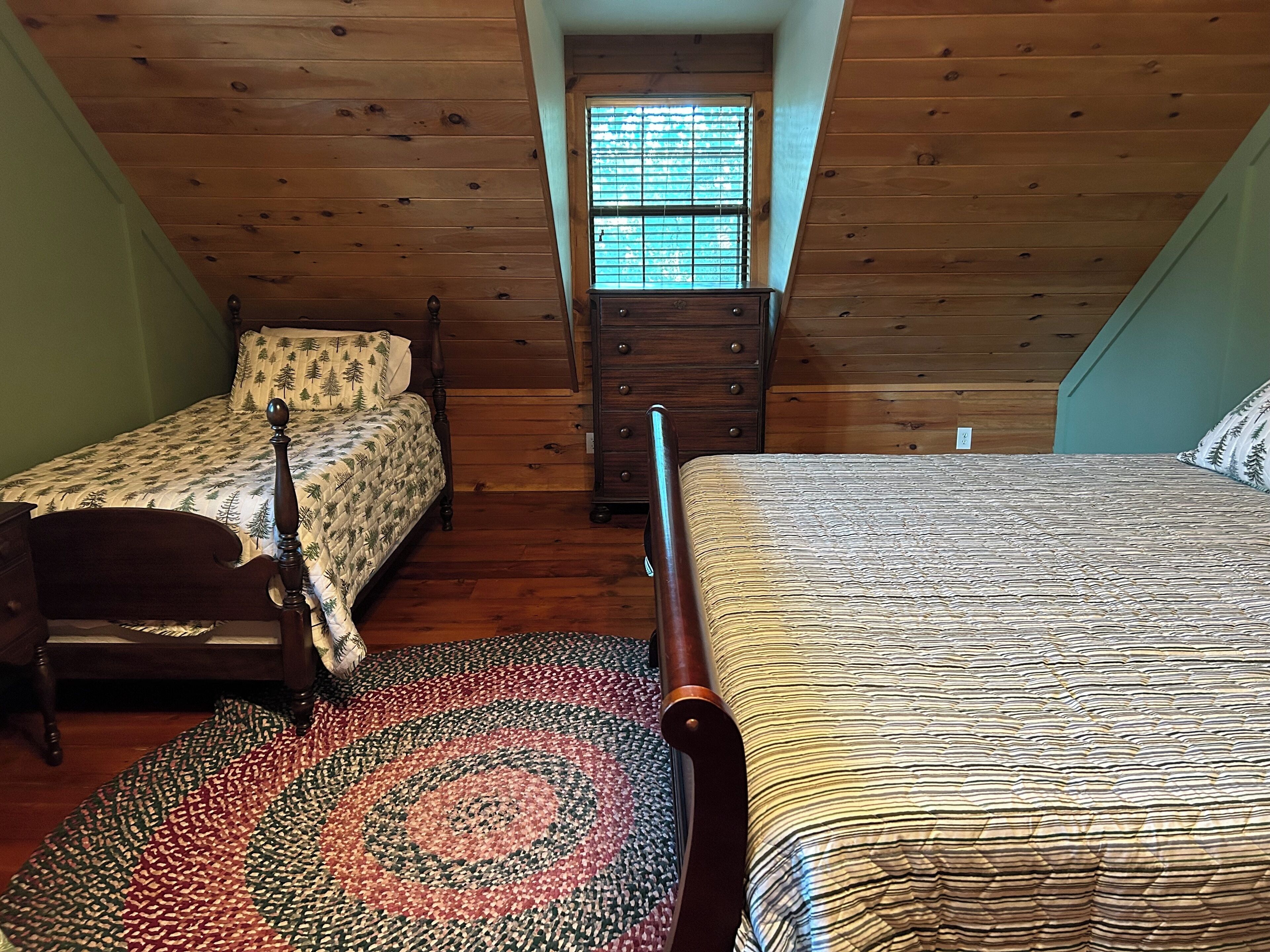 Quarto com duas camas individuais, uma cômoda de madeira e uma janela com persianas.