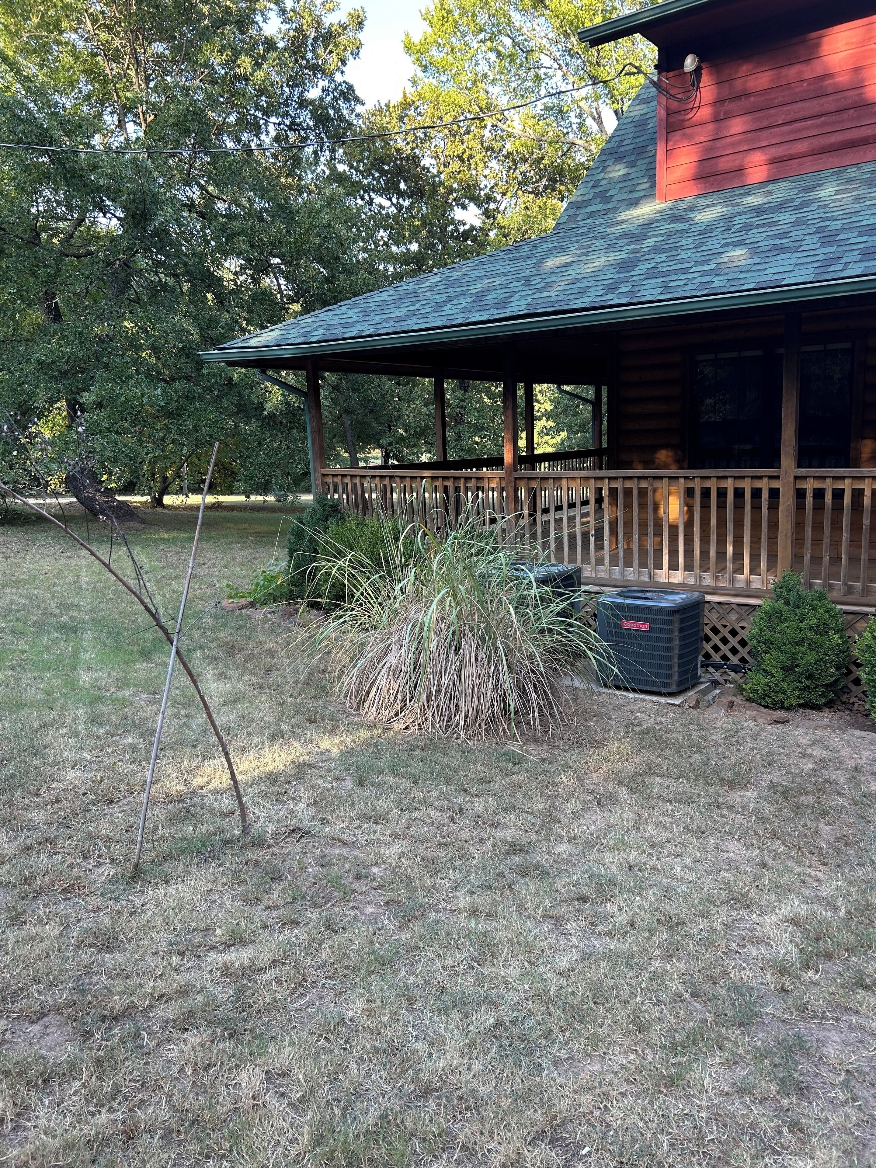 Une cabane en bois dotée d’un porche couvert, entourée d’une cour verdoyante et d’arbres.