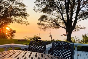 A deck with a table and chairs, overlooking a sunset with trees in the background.
