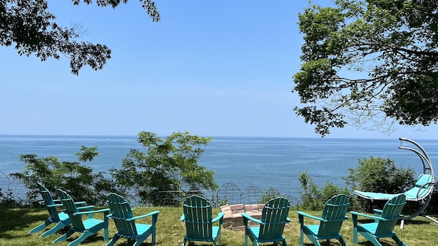 Ein grüner Außenbereich mit Rasen, Sitzgelegenheiten und einem Schaukelstuhl mit Blick auf ein Gewässer.