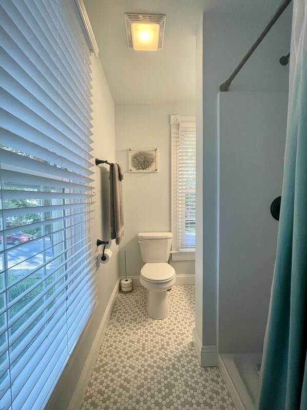 Une salle de bain avec des toilettes, une douche et une fenêtre équipée de stores.